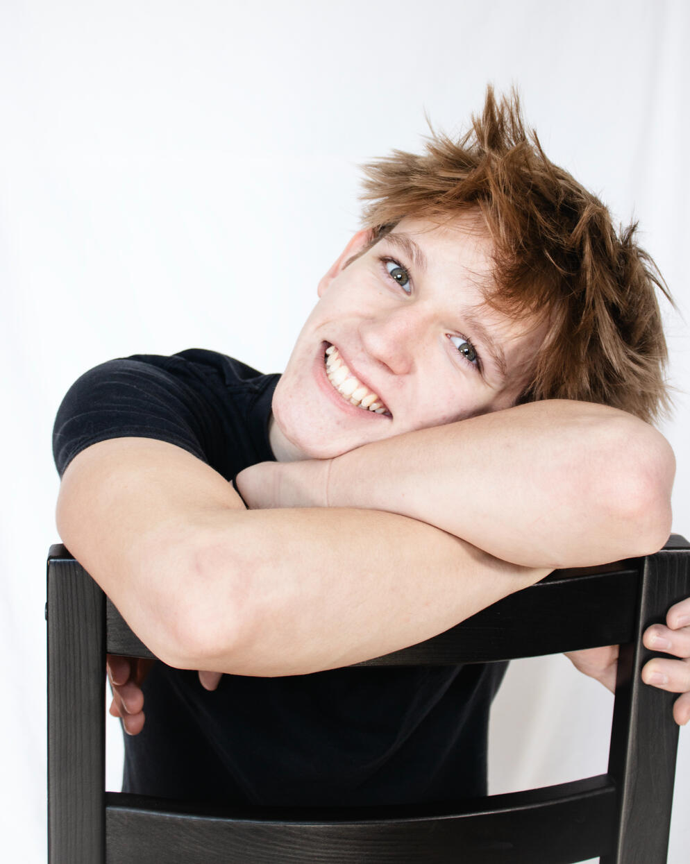 Blond teenage boy resting on his arms on the back of a chair